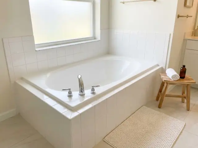 Illustration: glossy white bathtub with a white tile surround in a bright bathroom