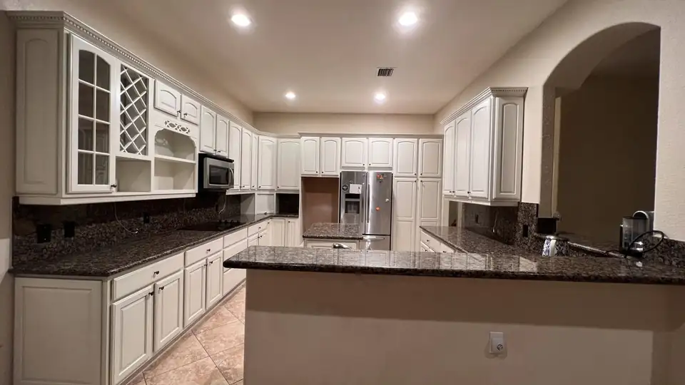 Kitchen with white cabinets, glass-front uppers and a dark granite island by Luxury Refinishing, which also offers bathroom refinishing in Miramar, FL